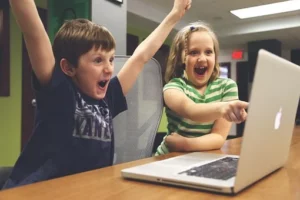 2 enfants qui regarde l'écran d'un ordinateur en levant les bras